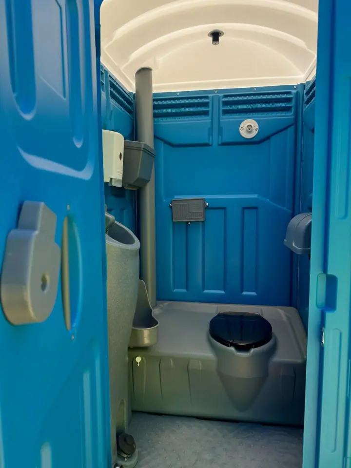 Inside a deluxe porta potty with a foot-pump sink and toilet