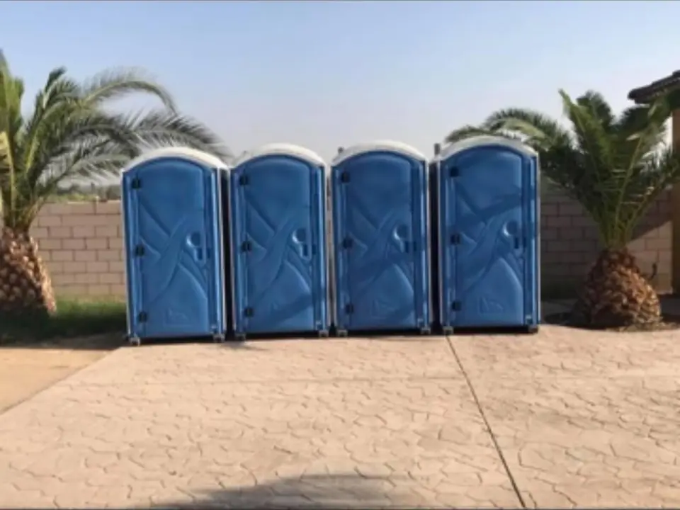 Four blue standard porta potties lined up on a paved lot