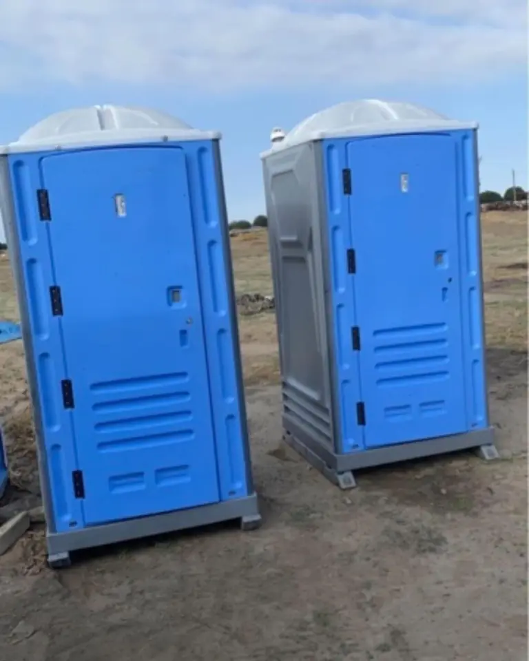Two standard porta potties on a dirt jobsite